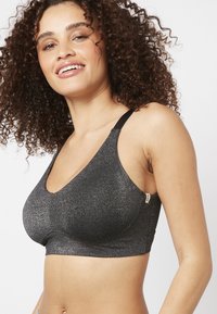 Top sportivo nero scintillante con design a V, spalline regolabili e un ampio elastico sotto il busto. Texture morbida con una leggera lucentezza.