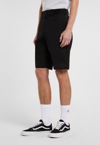 Black shorts made of sturdy fabric, featuring a belted waist, relaxed fit, and side pockets, paired with black sneakers and white socks.