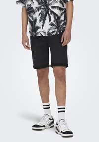 Pantaloni scurți negri, răsuciți, dintr-un material respirabil, asortați cu șosete albe cu dungi negre și pantofi sport negri/albi.
