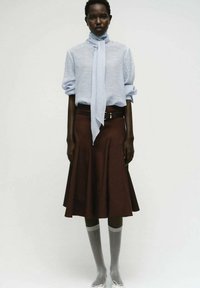 Camicetta in lino azzurro chiaro con una sciarpa abbinata, abbinata a una gonna svasata marrone. Calze grigie fino al ginocchio e scarpe di colore chiaro completano l'outfit.