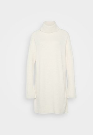 Un pull col roulé blanc fabriqué en matériau tricot doux. Il présente des manches longues et une coupe décontractée, avec une texture côtelée au niveau du cou et des poignets.