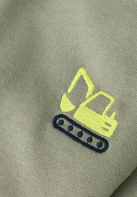 Wyszywany wzór żółtego koparki na jasnoszarej tkaninie. Koparka ma gąsienice i detale podkreślone granatową nicią.