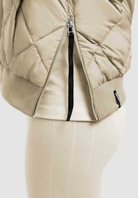 Beżowa pikowana kurtka z zamkiem błyskawicznym, ściągaczami na rękawach oraz jednolitą, teksturowaną podszewką.