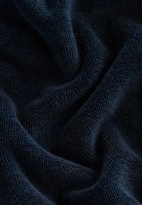 Tessuto in spugna color blu navy con una superficie texture, che mostra un tessuto morbido e peloso con motivi di tessitura pronunciati e pieghe delicate.