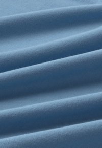 Tissu doux bleu clair avec des plis diagonaux subtils mettant en valeur la texture lisse et le tissage fin en maille.