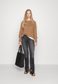 Bruine gebreide trui, witte blouse eronder, donkergrijze jeans met sleuven, zwarte gewatteerde totebag en sandalen met houten hakken.