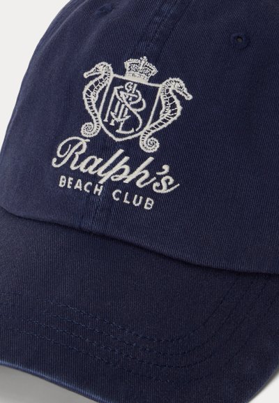 Șapcă bleumarin cu emblemă albă brodată, cu doi căluți de mare, o coroană și textul „Ralph's Beach Club” pe panoul frontal.