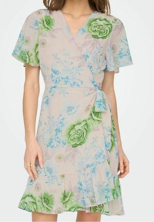 Femme portant une robe portefeuille beige clair à manches courtes avec un imprimé floral vert et bleu et un lien à la taille.
