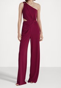 Burgundy yksiolkaiminen haalari, jossa on solmittu vyötärö ja leikattu sivu, valmistettu sileästä kankaasta. Housut ovat leveät lahkeet, ja ne ovat virtaavat.