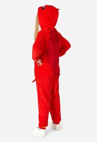 Rood pluche hooded onesie met een textuur aan de achterkant en een staartdetail. Bevat zakken en elastische manchetten. Draagt met witte sneakers.