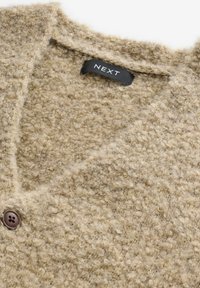Beige strikket cardigan med et struktureret, fuzzy stof. Har en V-udskæring, en brun knaplukning og en sort "NEXT" etiket indeni.