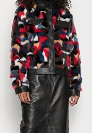 Veste en fausse fourrure patchwork colorée avec bordure en cuir noir portée avec une jupe en cuir noir, montrant le torse et les bras d'une personne.