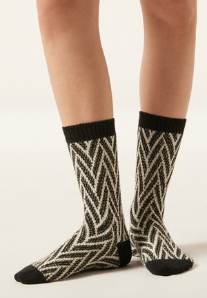 Schwarze und cremefarbene Socken mit diagonaler Chevron-Musterung, ausgestattet mit einem gerippten Strickbündchen sowie durchgehend schwarzen Zehen- und Fersenakzenten.