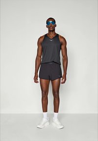 Šedý sportovní top bez rukávů a šortky, bílé tenisky a modré sluneční brýle. Jednoduchý design s pohodlným střihem a elegantní siluetou.