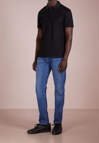 Černé polo tričko s límečkem, krátkými rukávy a knoflíkovou légou, v kombinaci se světle modrými džíny a černými šněrovacími teniskami.