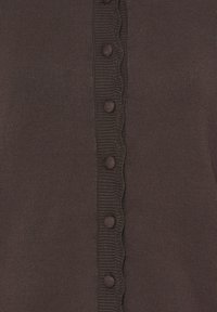 Tissu tricoté marron avec une rangée centrale de boutons ronds recouverts de tissu et un bord froncé le long de la patte de boutonnage.