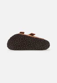 Brown sandal with dual velcro straps, textured black rubber sole featuring a wavy pattern, and a smooth upper section.
