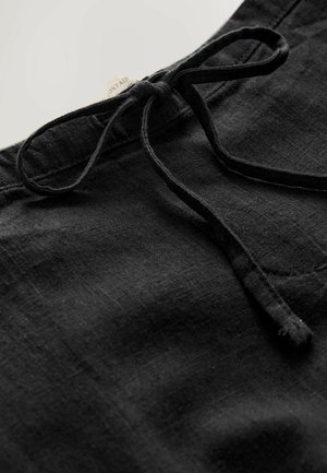 Mustat pellavashortsit, joissa on nyörivyötärö. Kangas on hienovaraisesti teksturoitu, jossa on sileä pinta ja vähäiset ompelujäljennökset.