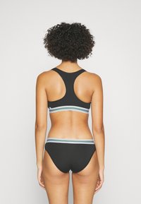Juodas bikini komplektas su lenktu viršumi, papuoštu daugiamačio juostelėmis, ir atitinkamais apatinius, išsiskiriantis sklandžia medžiaga ir minimalizmo dizainu.