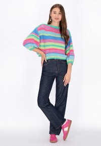 Maglione corto lavorato a maglia con righe orizzontali multicolori in rosa, verde e blu. Abbinato a jeans a gamba larga blu scuro e sneaker rosa.