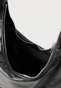 Μαύρη δερμάτινη τσάντα με ασημένιο φερμουάρ, που δείχνει ανοιχτή εσωτερική τσέπη με φερμουάρ και μια μικρή ετικέτα Calvin Klein.