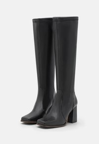 Bottes noires montantes en cuir lisse avec un bout carré et un talon épais, présentant un minimum de couture pour un design épuré.