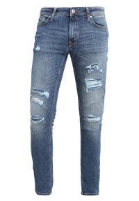 Slim-fit denim jeans i medelblått med slitna områden och flera hål. Tillverkade av bomull med en mjuk textur och traditionell femfickorsdesign.