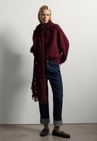 Jersey burdeos con un bufanda texturizada caída al rededor del cuello, combinado con jeans oscuros enrollados y mocasines marrones.