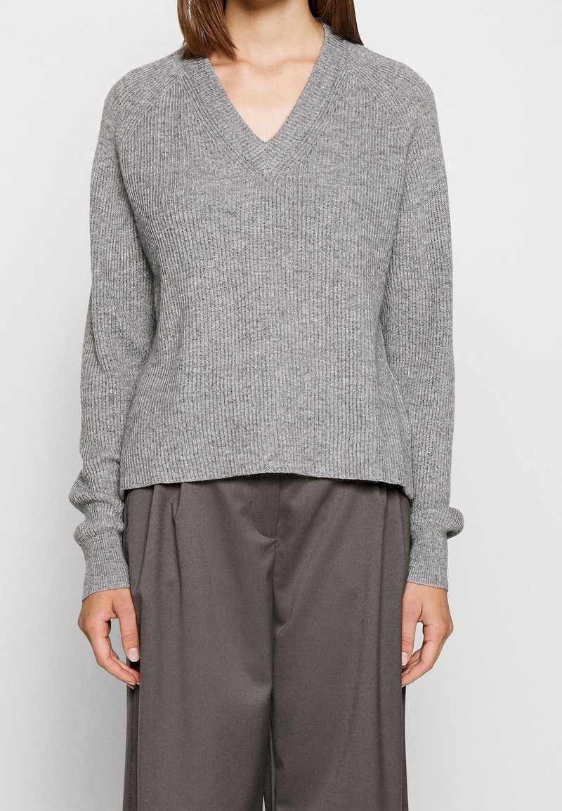 Maglione grigio a coste con scollatura a V e maniche lunghe, caratterizzato da un orlo leggermente corto e una finitura con texture. Abbinato a pantaloni grigi.