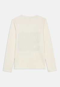 Μακρυμάνικη μπλούζα σε κρεμ χρώμα, φτιαγμένη από μαλακό ύφασμα, με στρογγυλή λαιμόκοψη και ίσια γραμμή, χωρίς ορατές εκτυπώσεις ή λεπτομέρειες.