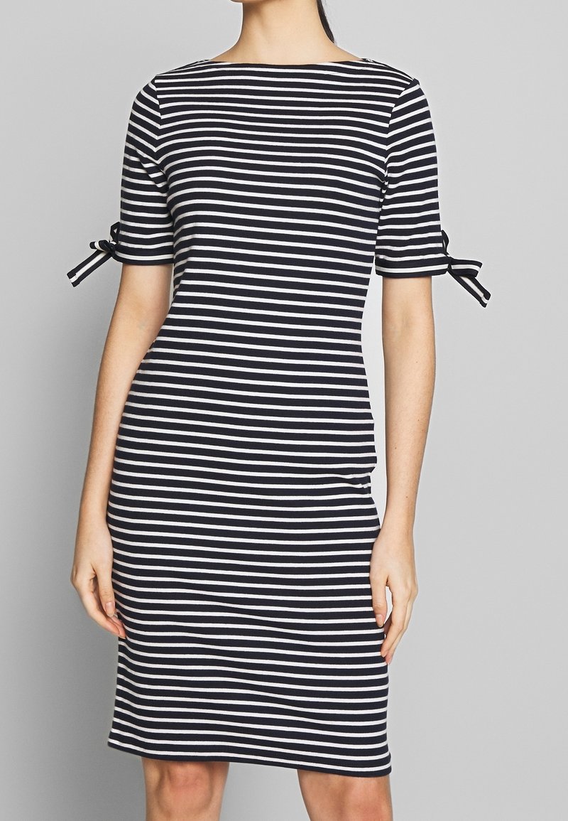 Vestido a rayas blancas y negras con escote redondo, mangas cortas y detalle de lazo en los puños. Diseño ceñido al cuerpo, longitud hasta la rodilla.