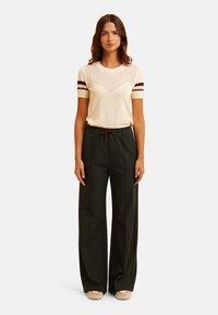 Cream short-sleeve sweater with mesh detailing and maroon stripes, paired with high-waisted dark green wide-leg trousers featuring a drawstring.