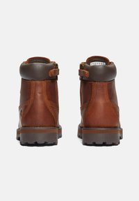 Botas de tobillo de cuero marrón con un cuello acolchado marrón, cierre de metal y suela de goma gris resistente. Presentan costuras en contraste y acentos laterales.
