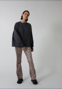 Szürke, túlméretezett, leengedett vállú pulóver bézs színű, leopárdmintás, bő szárú nadrággal kombinálva. A modell fekete platform csizmán áll.