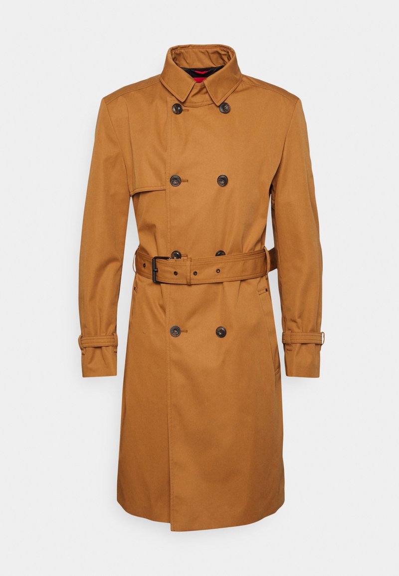 Cappotto trench marrone realizzato in tessuto liscio, con una chiusura doppiopetto, cintura e polsini con bottoni. Collo classico con cuciture in evidenza.