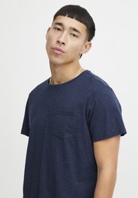 Námořnické modré bavlněné tričko s krátkými rukávy, kulatým výstřihem a kapsičkou na prsou. Tkanina má tečkovanou strukturu.