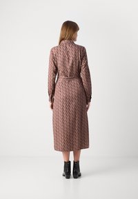 Donna in piedi di spalle, indossa un abito midi a maniche lunghe con motivo, una cintura e stivali neri alla caviglia su uno sfondo bianco.