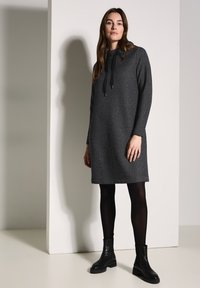Graues Hoodie-Kleid mit strukturiertem Muster und verstellbarem Kapuzenzug. Trägt man mit schwarzen Leggings und Stiefeln. Geschmeidiger Stoff und lockere Passform.