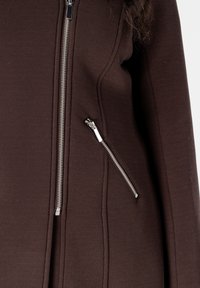 Bruine ritsjack met textuurstof, voorzien van een zijritszak en metallic ritssluitingen aan de voorkant.