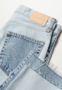 Vaqueros de mezclilla azul claro con un lavado medio, que cuentan con una etiqueta de cuero que dice "BLUE EDITION" y detalles de dobladillo deshilachado.