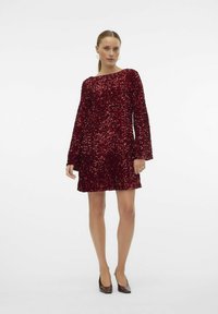 Punane sädeleva kleit pikkade kellukesleevestega ja paadi kaelusega. Tekstuurne pind särab valguse käes. Lühike, A-line siluett.