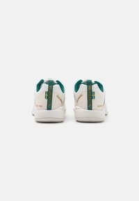 Hvite atletiske sko med teal-detaljer, teksturert stoff, merkevareinformasjon og hylletrekksløyfer. Har et slankt, minimalistisk design.