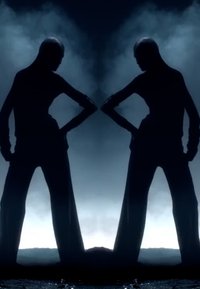 Black silhouette of two figures standing back-to-back. They wear fitted clothing with wide, flared pants and have arms posed on hips.