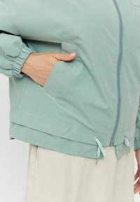 Lättvikts, mintgrön jacka med elastiska ärmslut, dragkedjestängning och justerbar nederkant. Har sidofickor och kontrasterande dragskoaccent.