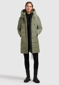 Olīvu zaļš pildīts mētelis ar kapuci, priekšējais rāvējslēdzis, pogas un regulējama virve. Gluda tekstūra ar horizontālu quiltēšanu.