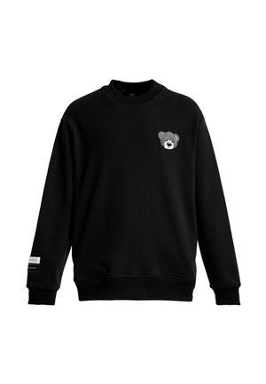 Sudadera negra con cuello redondo y mangas largas, con una pequeña cara de oso de peluche gris bordada en el pecho izquierdo y una etiqueta en el puño de la manga izquierda.