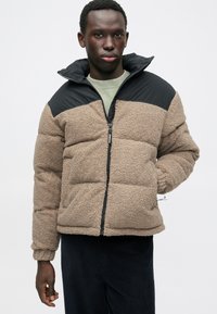 Jachetă din fleece cu textură bej, panouri de umăr din nailon negru, închidere cu fermoar, design căptușit și manșoane elastice. Potrivită pentru vreme rece.