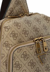 Borsa in tessuto beige con motivo strutturato, dotata di cerniere e dettagli con logo in tonalità oro. La forma è compatta con un design triangolare.