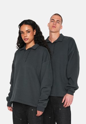 Dark gray oversized polo sweatshirts with a collar, featuring a subtle vertical text design on the front. Smooth texture, casual fit.
