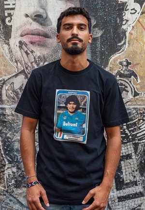 Zwarte katoenen t-shirt met een vintage afbeelding van een voetballer, blauwe trui met "Buitoni," ingelijst ontwerp en de tekst "Napoli" erboven.